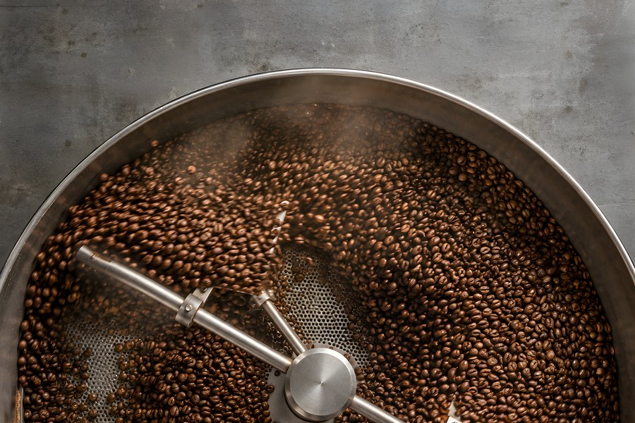 Roasted coffee beans swirling in a stainless steel cooling tray with a rotating rake arm and rising steam, overhead view
