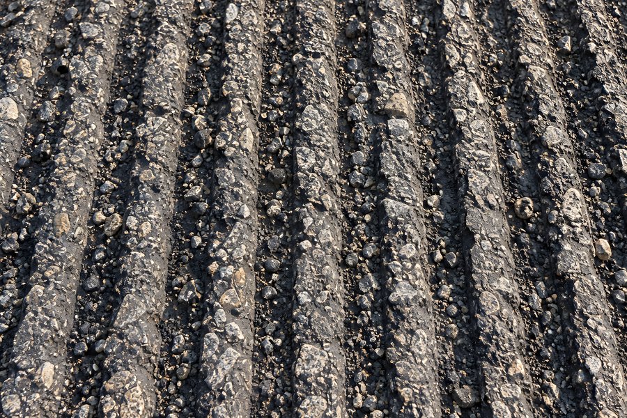 Close-up of grooved asphalt pavement with exposed aggregate stones, textured road resurfacing surface in sunlight