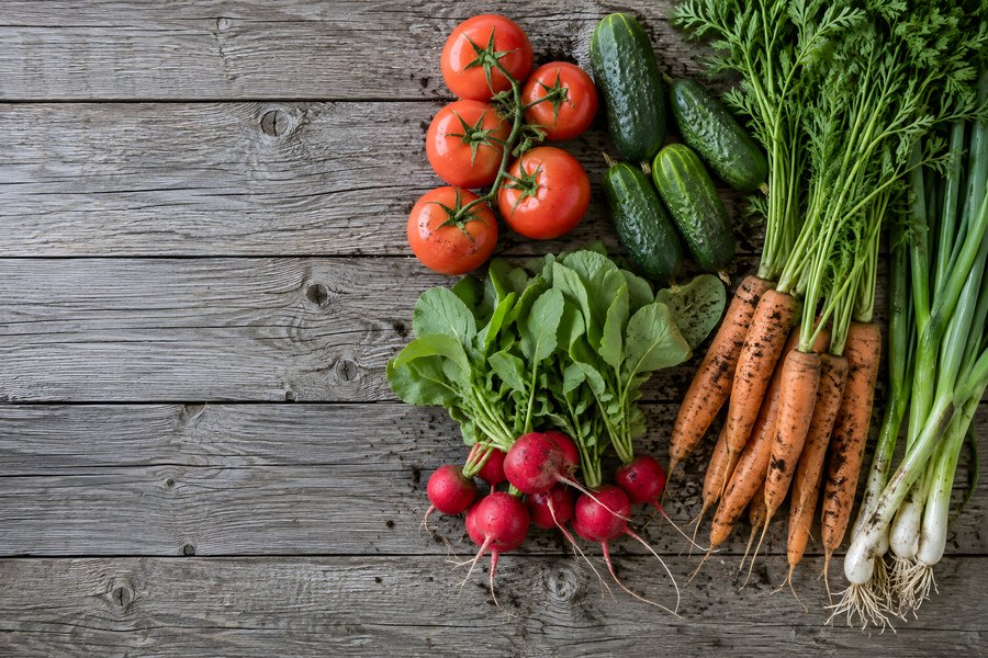 Overhead flat lay of fresh garden vegetables, tomatoes, cucumbers, carrots and radishes, on a rustic wooden table with copy space