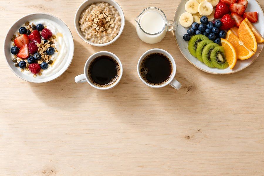 Overhead healthy breakfast table with yogurt bowl, oatmeal, fresh fruit, coffee and milk on a wooden surface with copy space