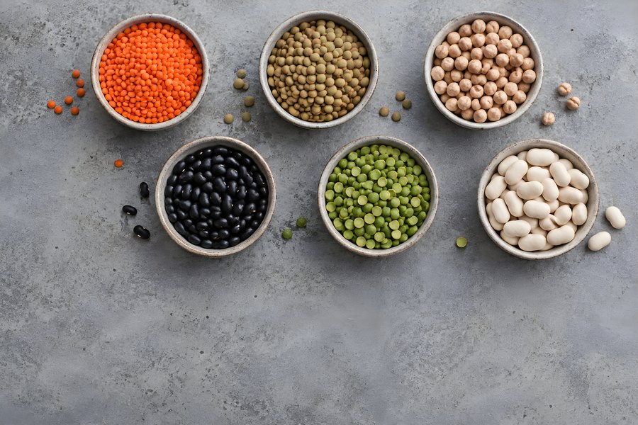 Assorted Dried Legumes in Ceramic Bowls – Red Lentils, Chickpeas, Black Beans and Split Peas on Gray Concrete with Copy Space
