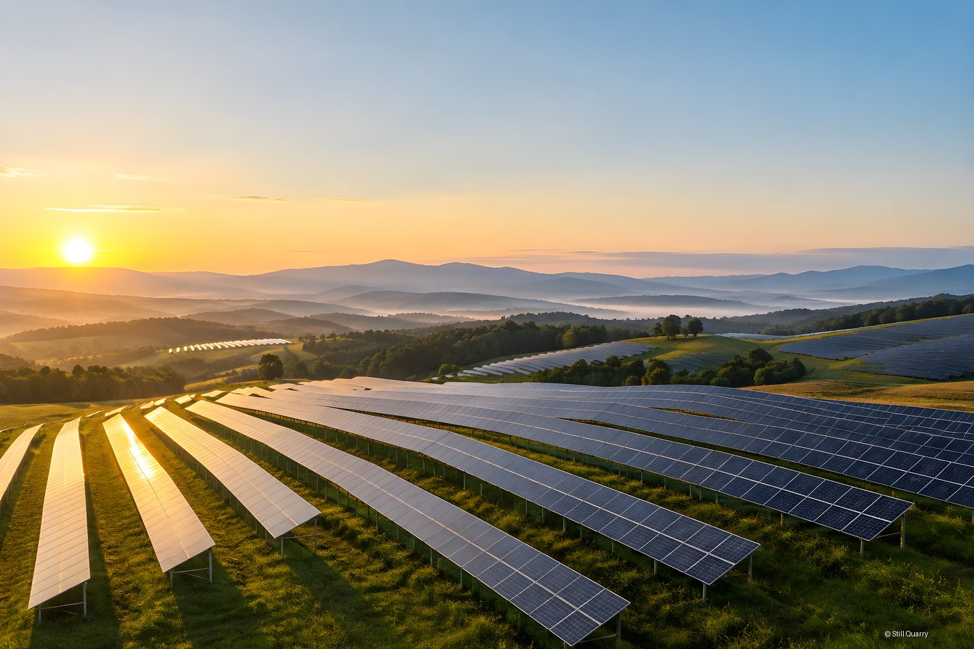 Aerial view of a utility scale solar farm on green rolling hills at sunrise with misty mountains in the distance