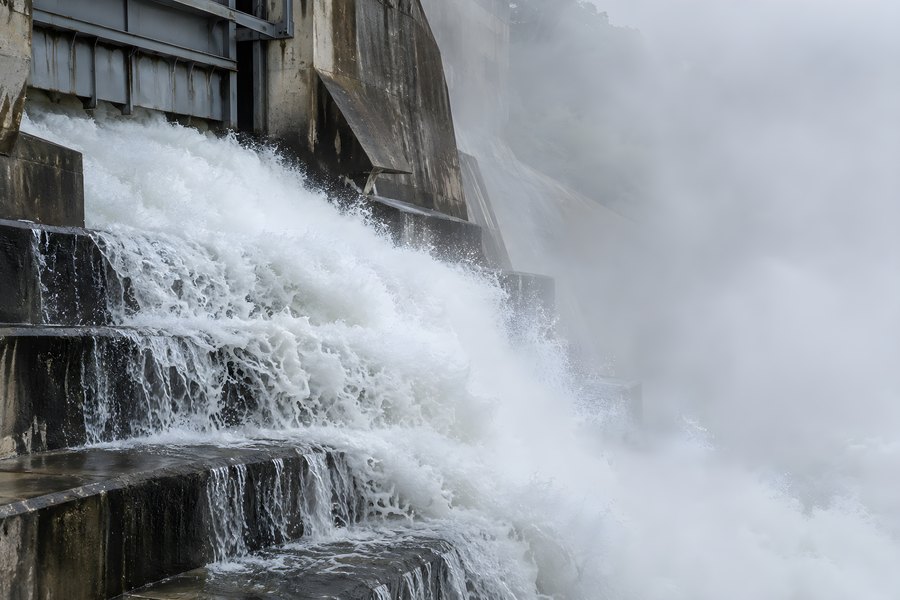 Powerful water discharge cascading down the stepped concrete spillway of a hydroelectric dam, wrapped in dense white mist and spray