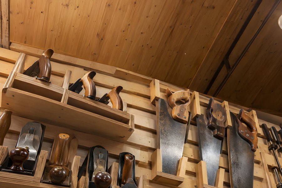 Organized workshop wall storing wood hand planes, backsaws, chisels and clamps beneath a vaulted wood ceiling, no people visible