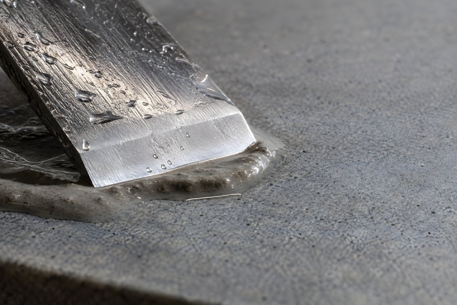 Close-up of a chisel blade edge resting on a wet whetstone with gray sharpening slurry