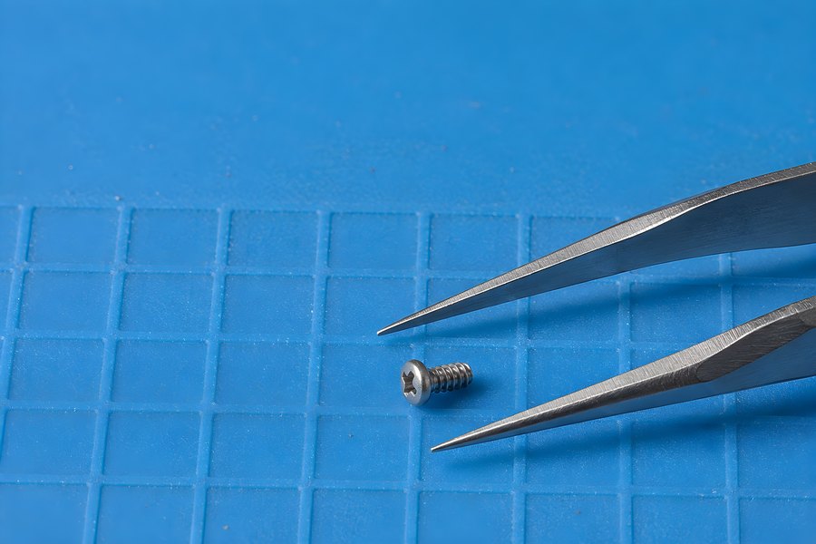 Precision Tweezers Picking Up a Tiny Phillips Screw on a Blue Grid Repair Mat