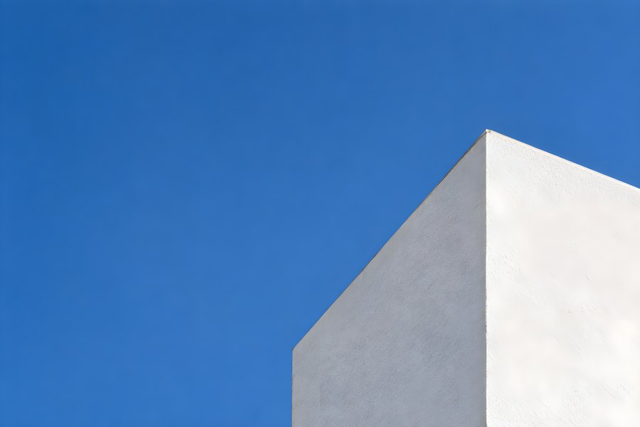 Minimal white building corner with diagonal roofline against a clear blue sky and large copy space