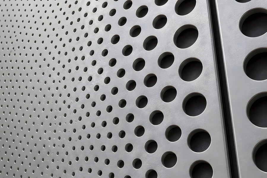 Perforated metal facade panel close-up with a gradient of round holes and a vertical seam joint between two grey cladding panels