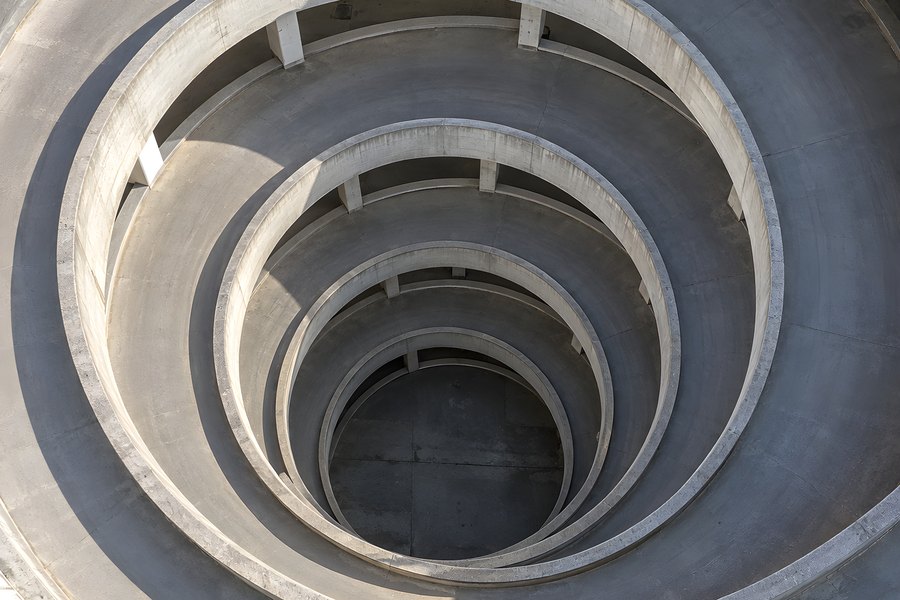 Aerial view into an empty spiral parking garage ramp with concentric concrete rings and columns